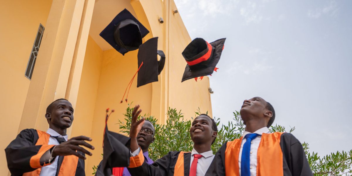 Four young men in black graduation robes tossing up graduation caps while smiling.