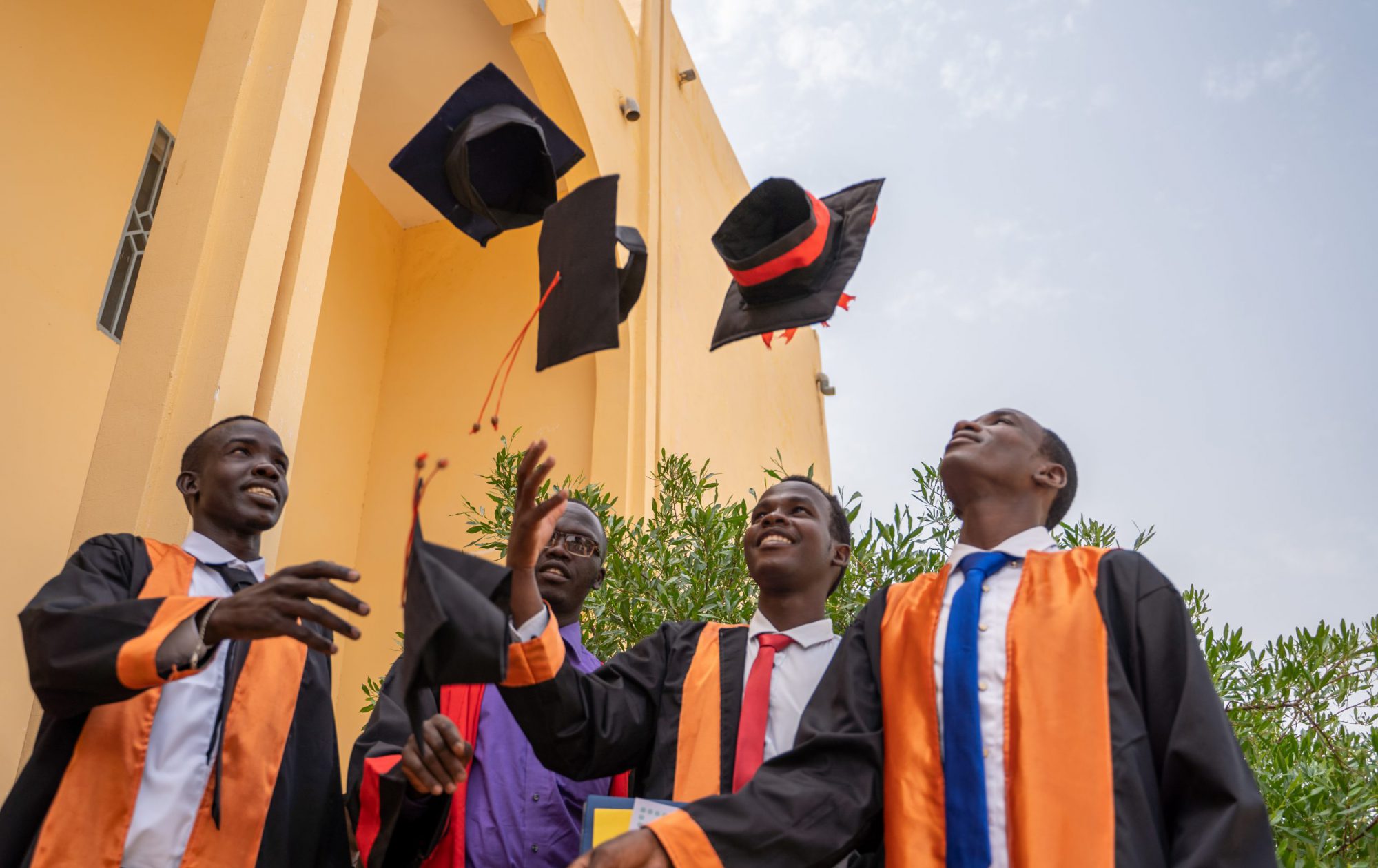 Four young men in black graduation robes tossing up graduation caps while smiling.