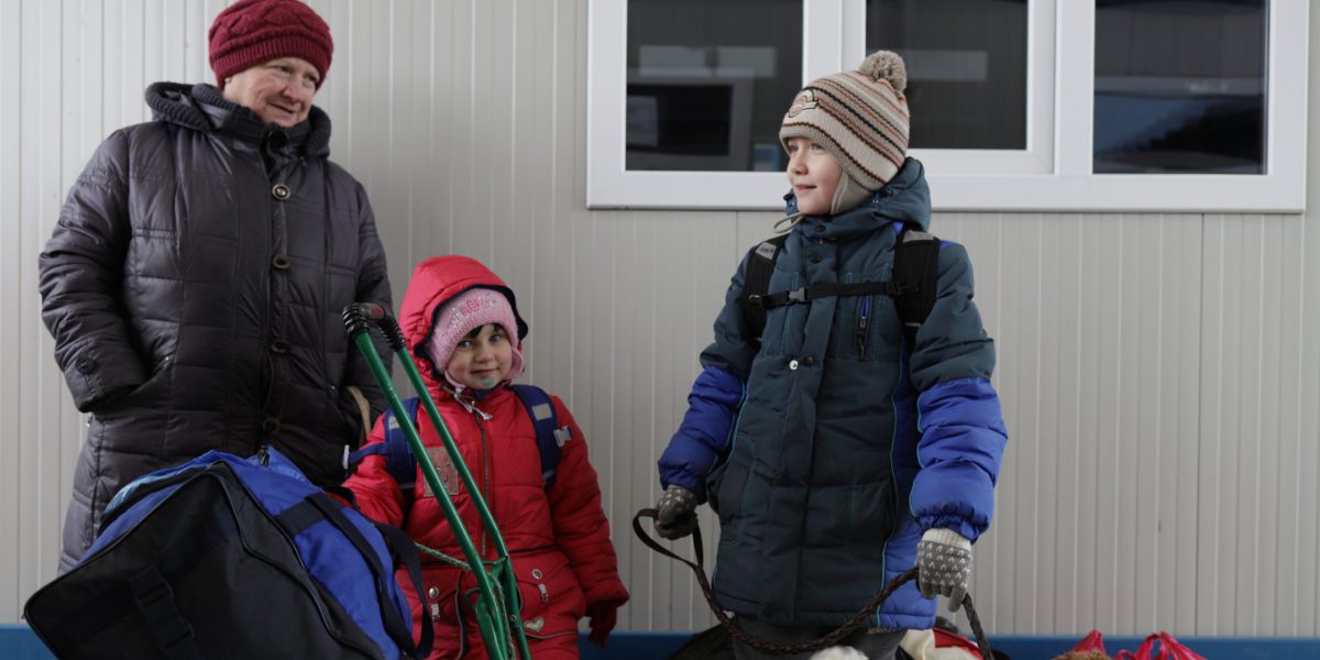 A man, a young boy, and a young girl standing together with coats and luggage, looking at the camera while holding a dog on a leash.