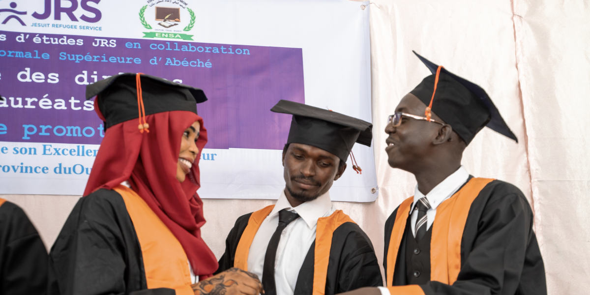 Three young adults, one woman and two men, stands around in graduation attire with graduation caps on.