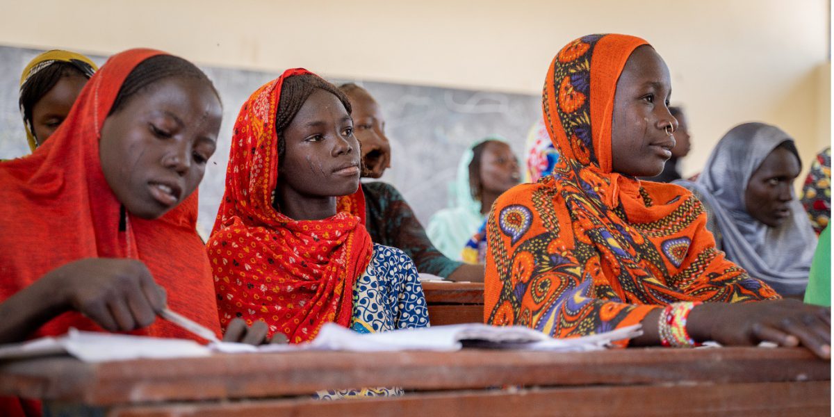 Three young women sitting at a desk doing what appears to be school work as they look ahead in front of them.