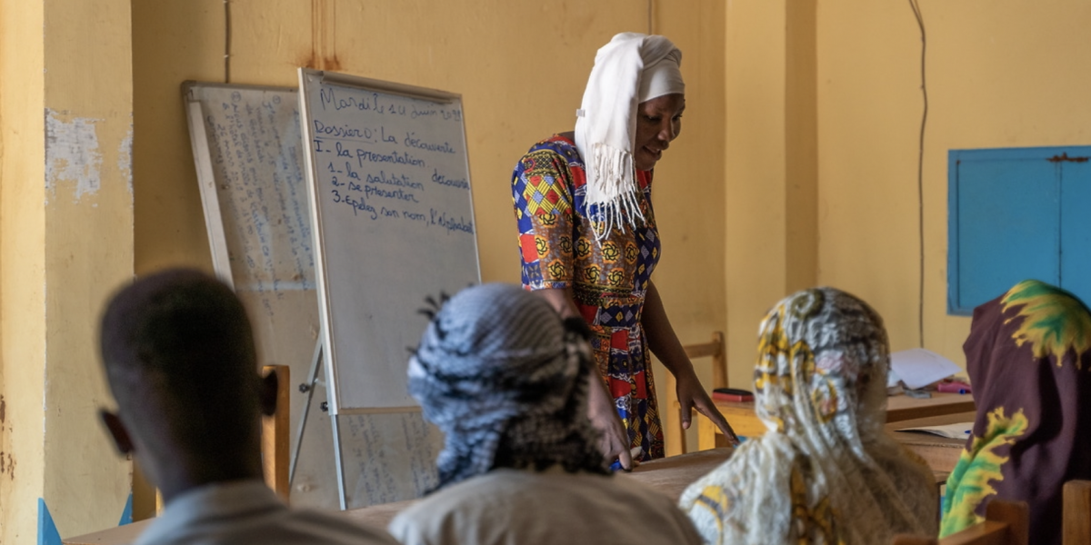 A woman standing by a standing note pad in front of a classroom of students.