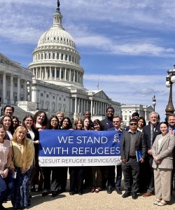 A group of advocates standing in front of the Unted States Capitol building while holding a blue and white banner that says, 