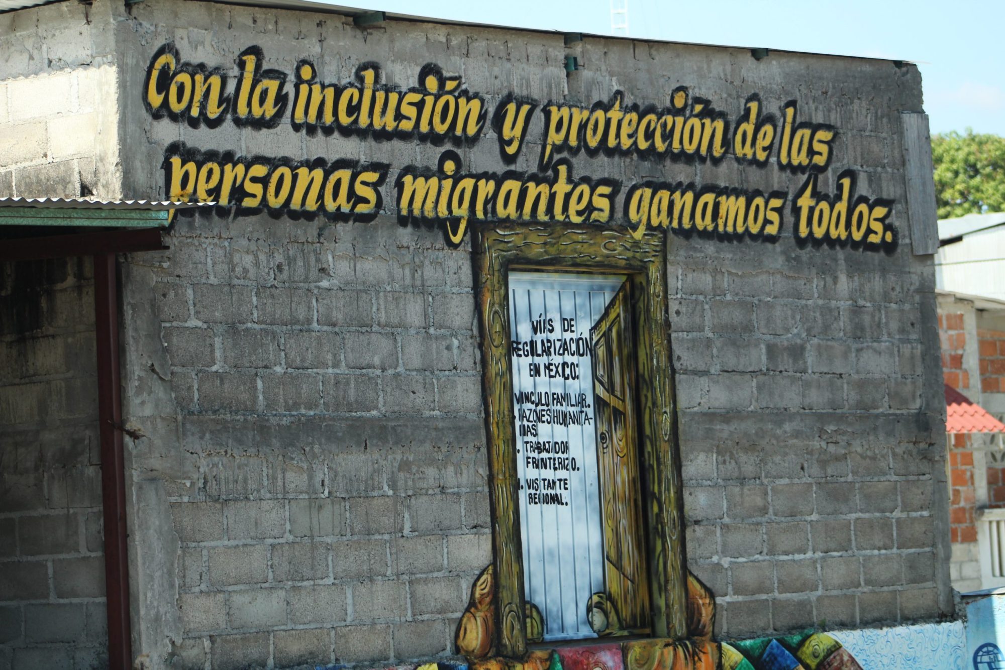 A wall mural that says: Con la inclusión y protección de las personas migrantes ganamos todos which translates to 