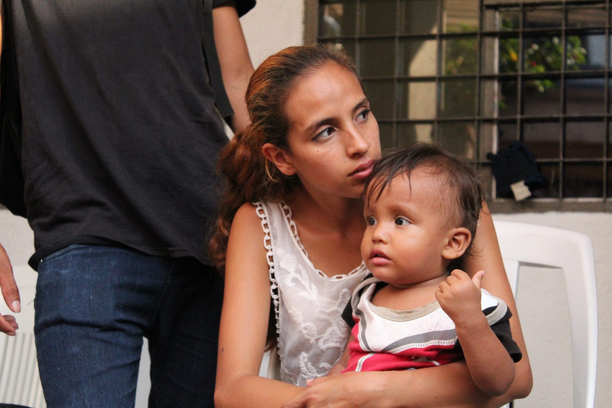 A migrant mother holds her child while waiting at a border crossing, symbolizing the strength and resilience of displaced families.