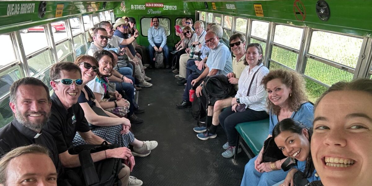 A group of people sitting inside of a bus, all are smiling ar the camera.