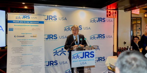 United Nations Secretary-General António Guterres Honored at JRS/USA 45th Anniversary Dinner. A man standing at a podium speaking to a small, intimate crowd. He is standing in front of a banner with the JRS/USA logo on it.
