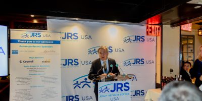 United Nations Secretary-General António Guterres Honored at JRS/USA 45th Anniversary Dinner. A man standing at a podium speaking to a small, intimate crowd. He is standing in front of a banner with the JRS/USA logo on it.