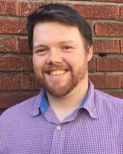 A man with dark hair smiling at the camera standing in front of a brick wall. | Ignatian Migration Dialogue, State and Local Immigration Measures