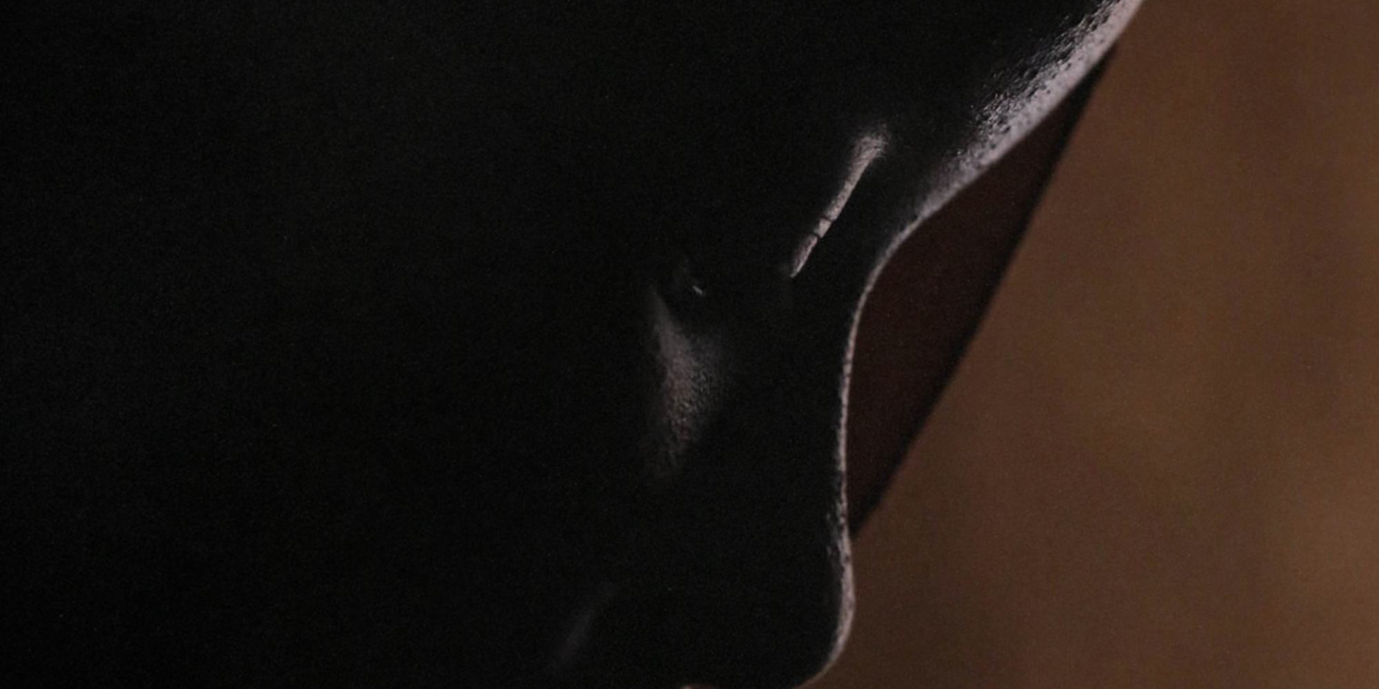 An up-close portrait of a person looking down in front of a brown background.