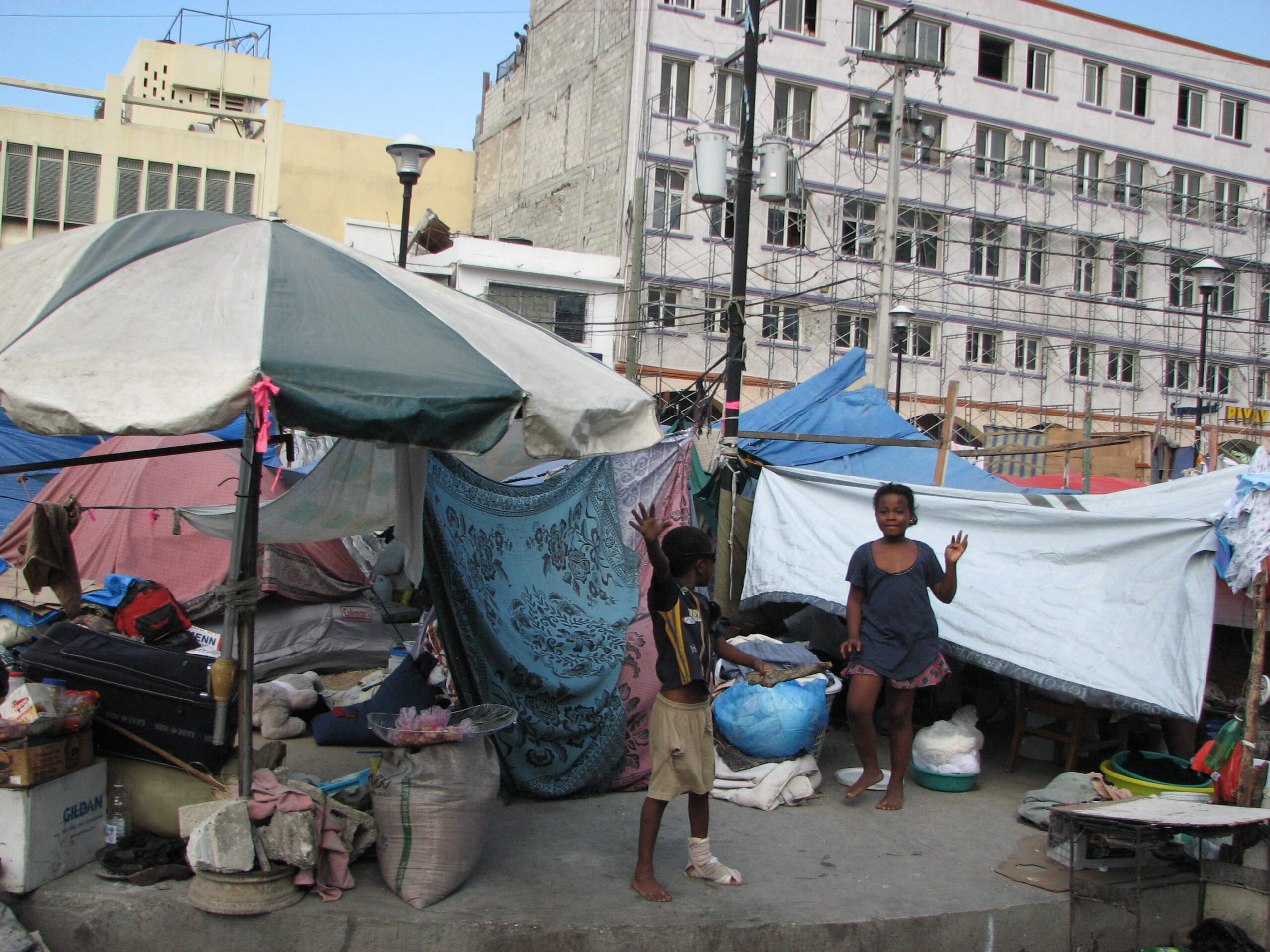 Two children standing in front of make shift shelters of tents in Haiti.