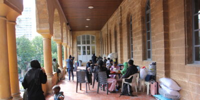 A group of people sitting on the ground outside of a church. St. Josephs Church opened up to accommodate refugees and migrants n Lebanon.