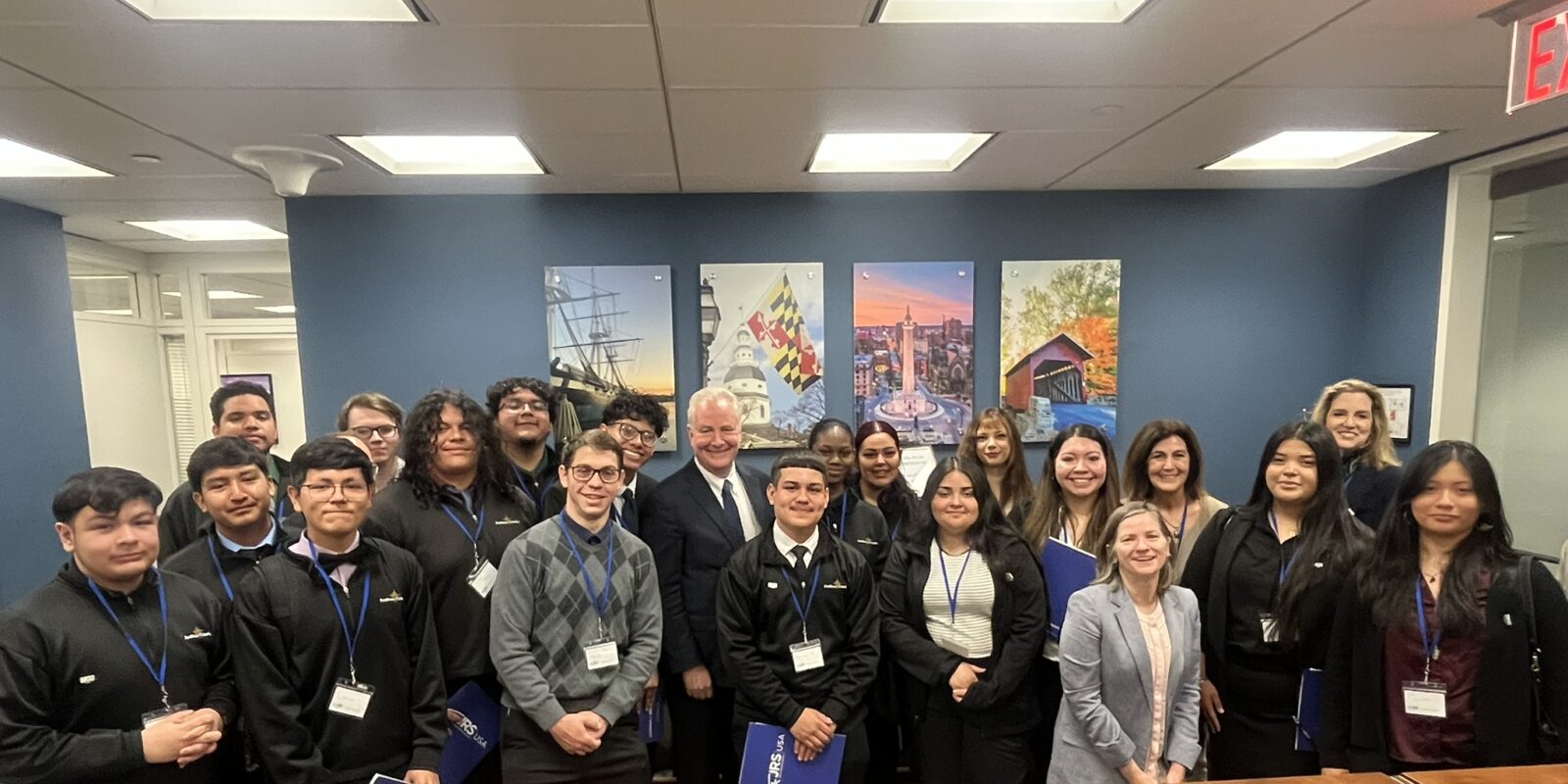 A group of people standing in a room all wearing business casual clothing. Each person has a JRS/USA Advocacy Day lanyard. They are looking at the camera smiling.