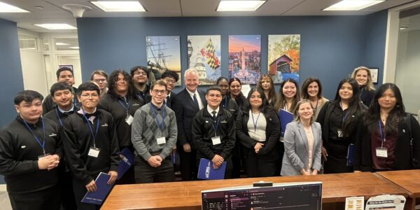 A group of people standing in a room all wearing business casual clothing. Each person has a JRS/USA Advocacy Day lanyard. They are looking at the camera smiling.