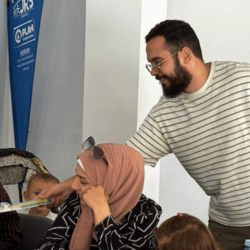 A man leaning over a woman while smiling. He is handing her a piece of paper. There is a JRS banner in the background.