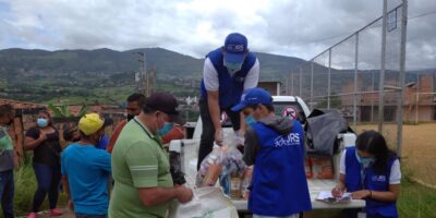 JRS humanitarian aid workers supporting refugees and other forcibly displaced people in Venezuela. There are people wearing blue vests with JRS on them, handing people different food items from a truck.
